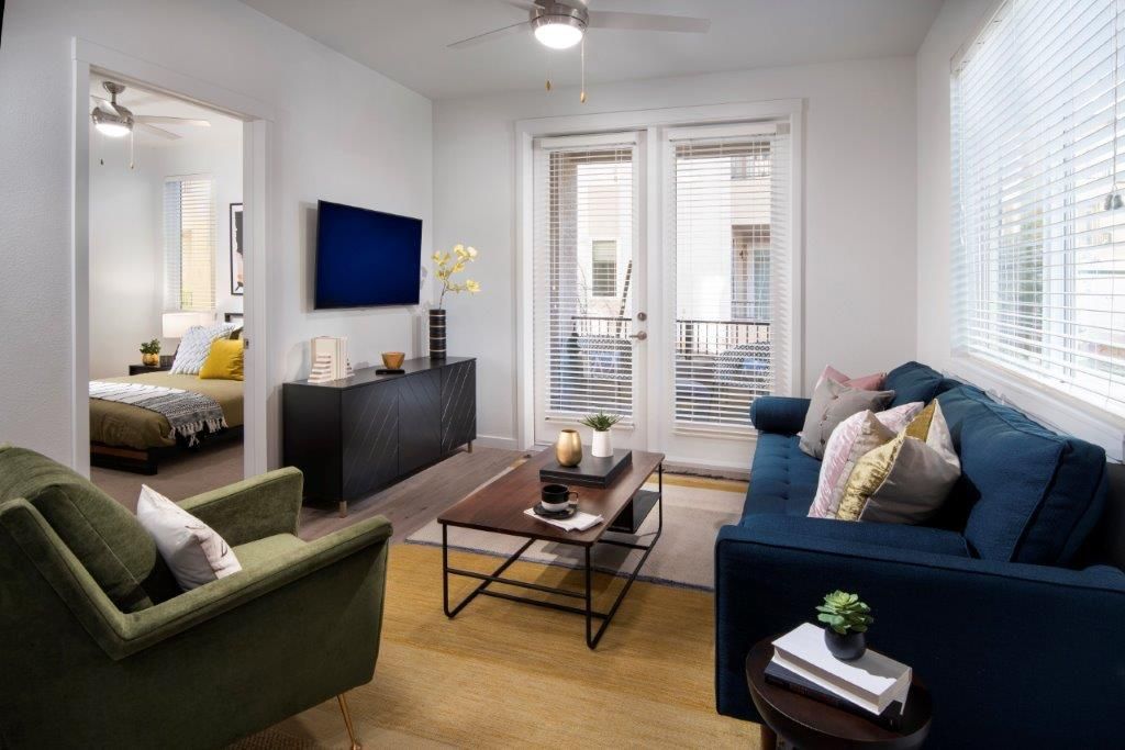 Living room in an apartment with a blue sofa, green chair, coffee table, TV, and balcony doors at Aiya, offering apartments in Gilbert, AZ.