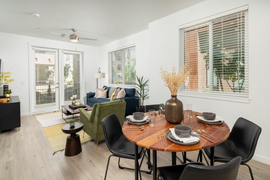 Open-concept apartment living and dining area with a round wood table, black chairs, and large windows at Aiya, offering apartments in Gilbert, AZ.