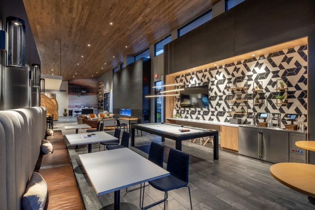 Interior of a modern apartment community lounge with tables, seating, a pool table, and a geometric wall at Aiya, offering luxury apartments in Gilbert, AZ.