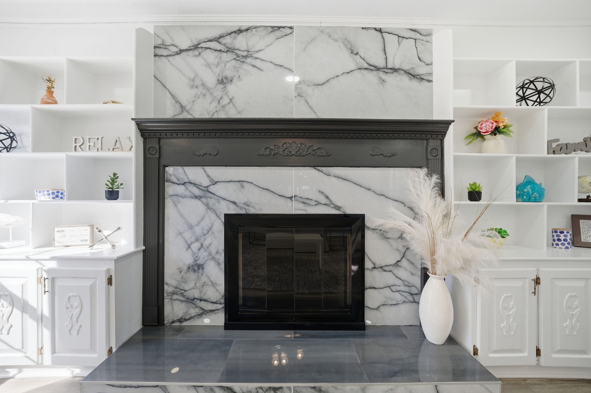 Modern white living room fireplace with gray marble surround, built-in shelves, and decorative accents