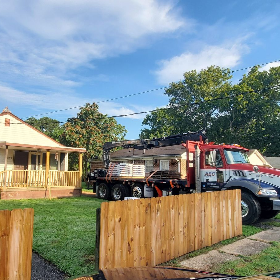 Red tow truck parked beside a house and wooden fence in a sunny yard