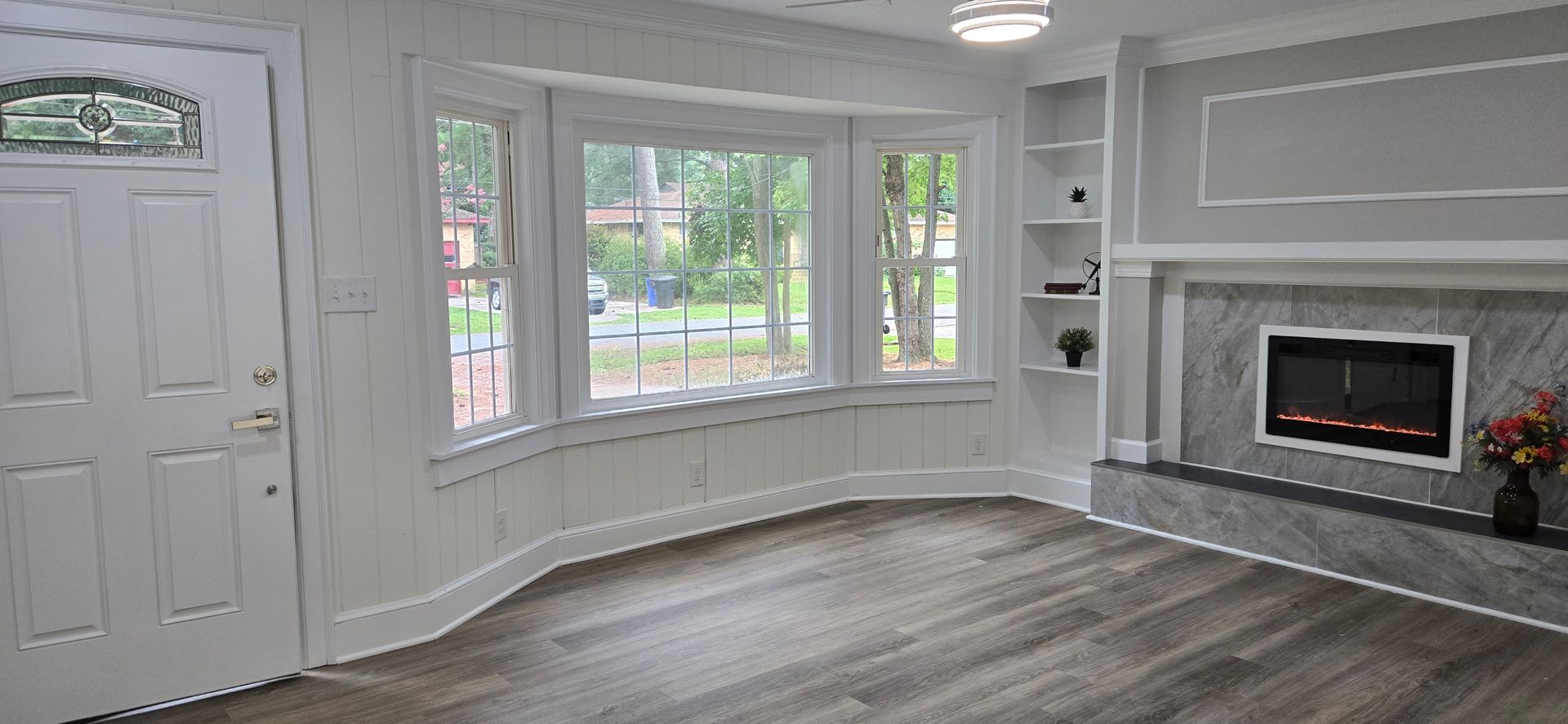 Bright living room with large windows, fireplace, and white front door with wood floors