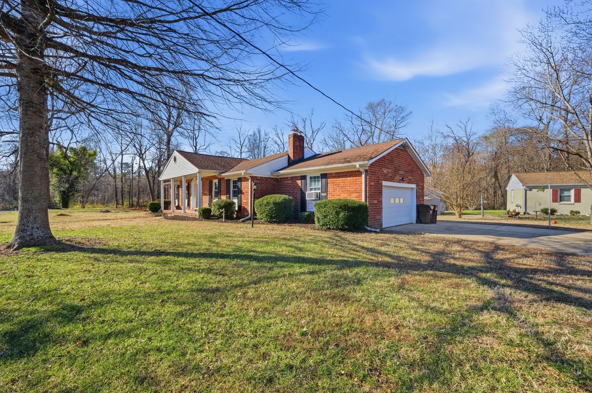 Brick house with red roof and white porch in a grassy yard under a clear blue sky