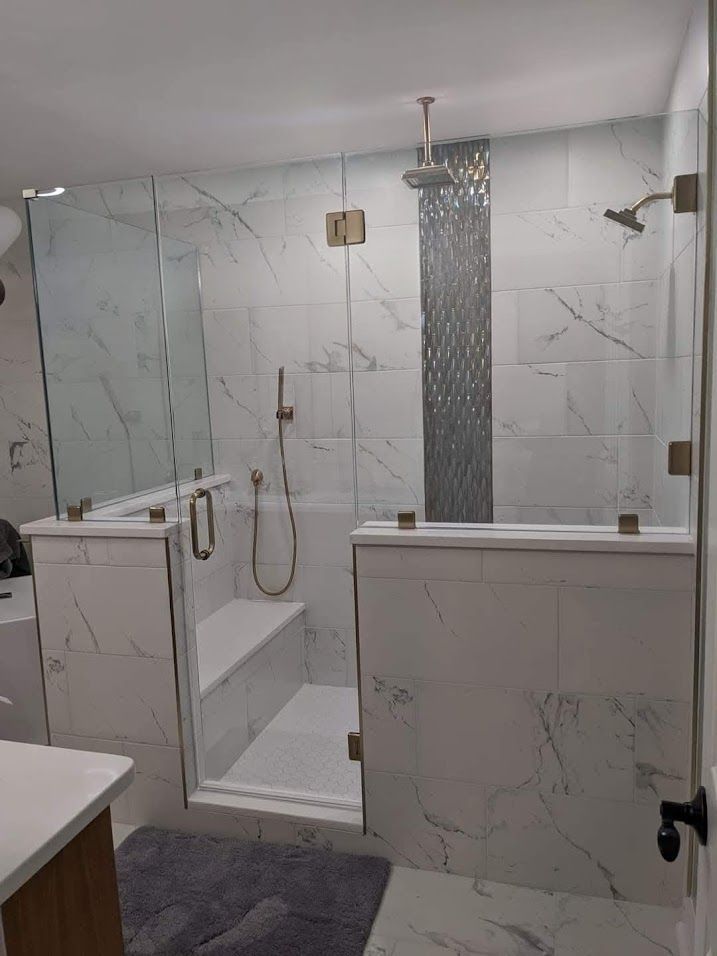 Modern white-tiled bathroom with walk-in shower, glass partition, and dark accent tile strip