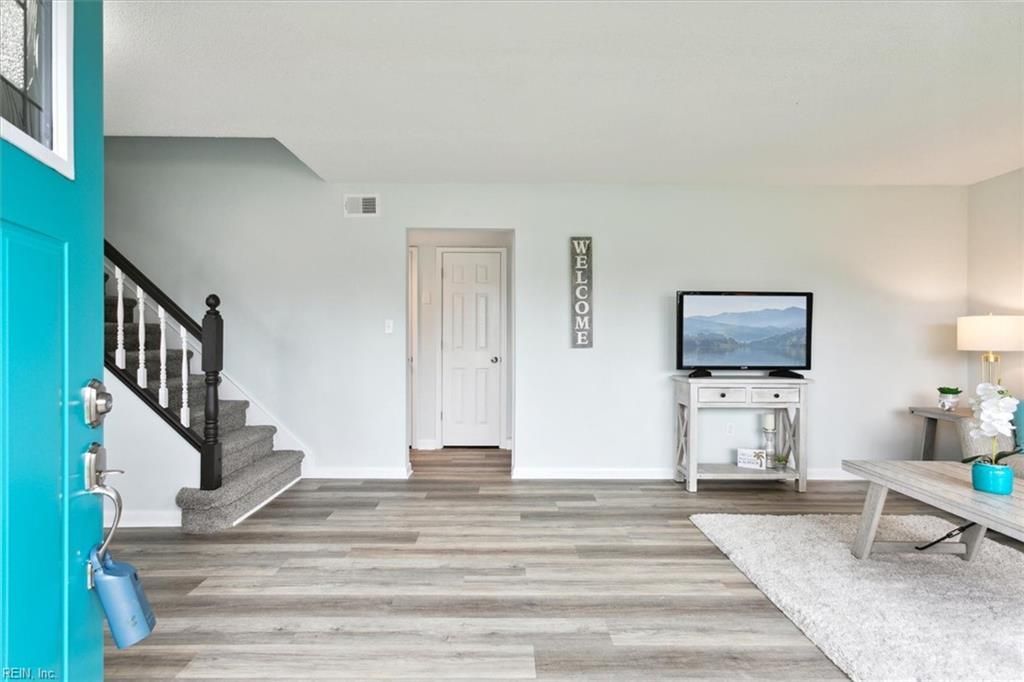 Bright living room with gray floors, stairs, white walls, and a TV on a stand near a couch and lamp.