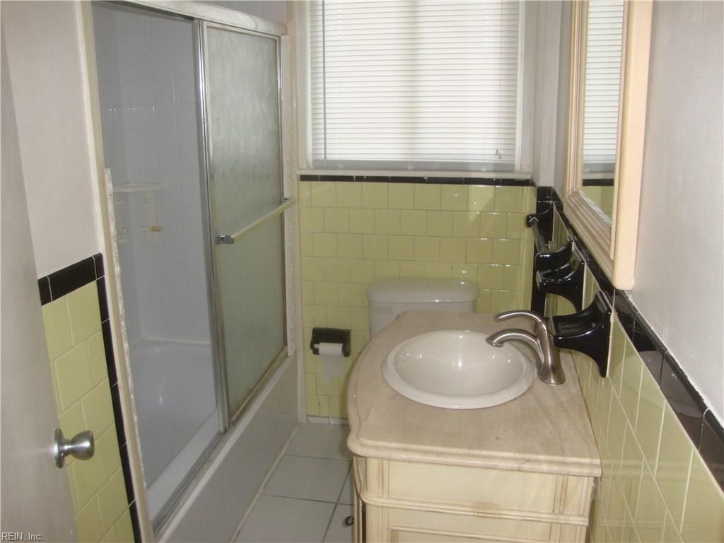 Small bathroom with a sink vanity, shower stall, and pale green tiled walls.