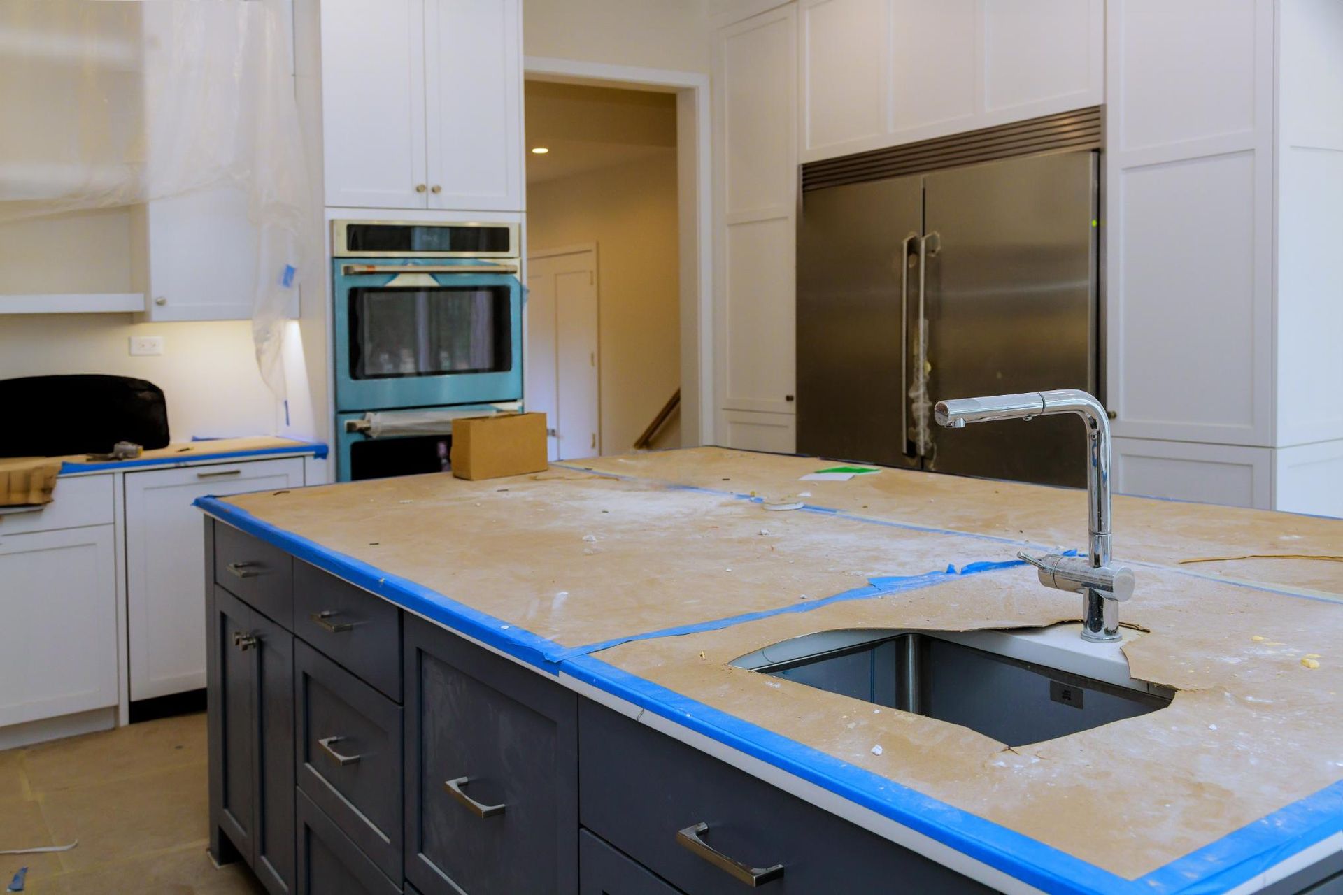 Kitchen with blue-gray island, white cabinets, stainless steel appliances, and protective coverings during renovation.