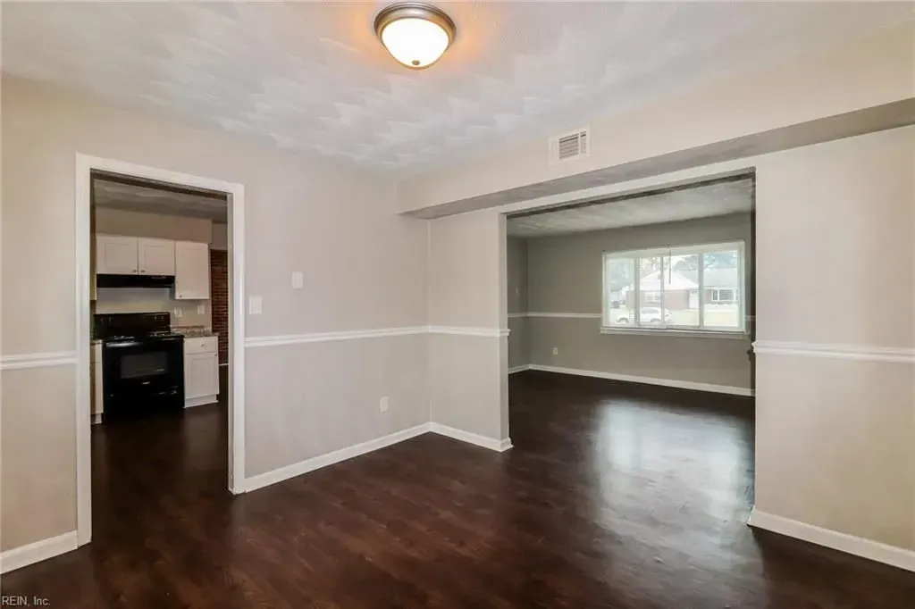 Empty beige living room with dark wood floors and large open doorway to a sunlit room