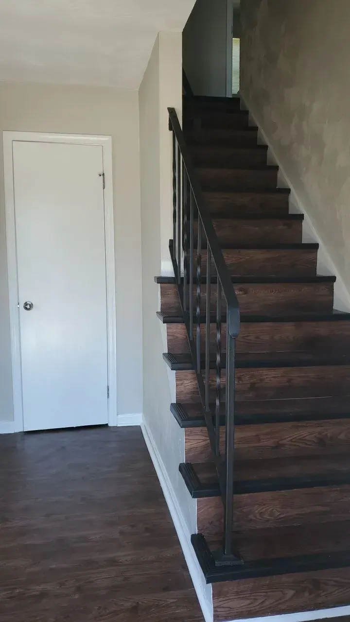 Interior hallway with dark wooden staircase, black railing, and white door on the left.