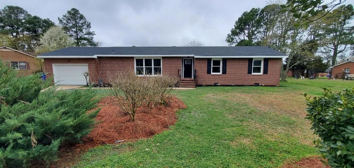 A brick ranch-style house with a garage door, windows, and a dark roof, on a cloudy day.