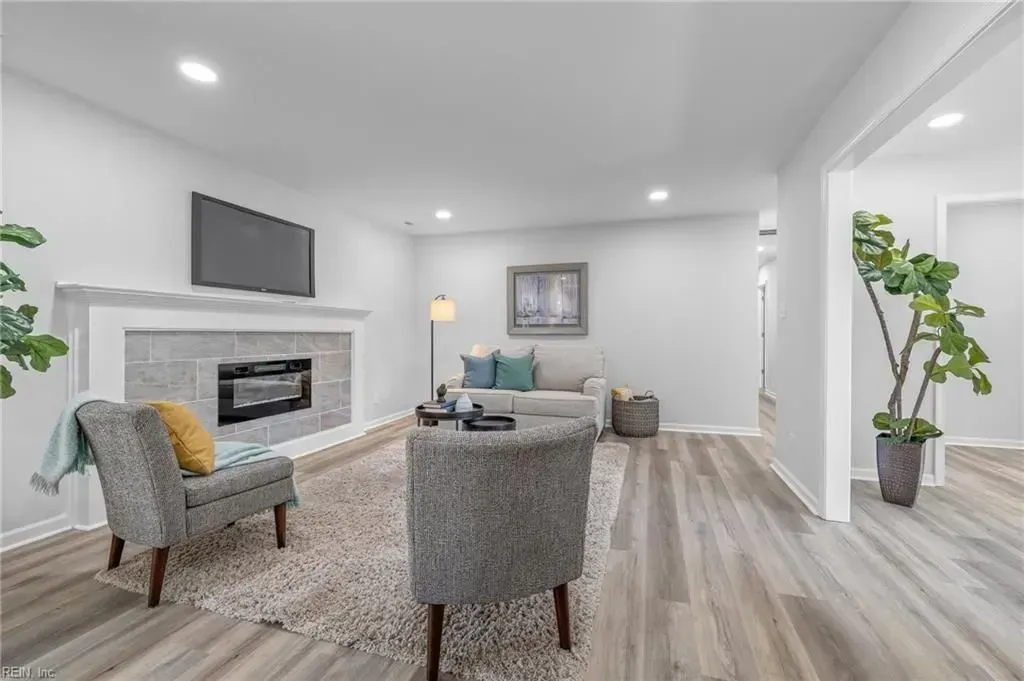 Bright modern living room with gray chairs, fireplace, wood floors, and indoor plants