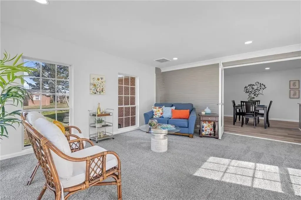 Bright living room with wicker chair, blue sofa, dining area, and sunlight on carpet.