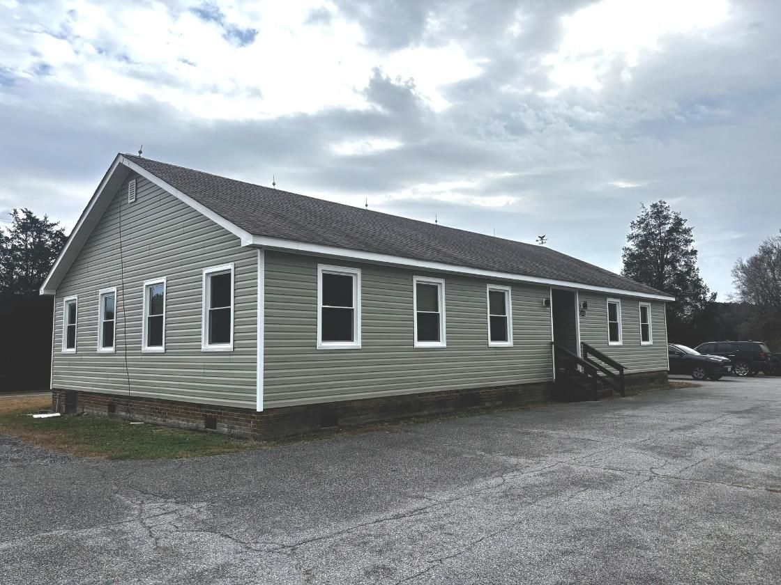 A one-story building with light green siding and multiple windows, under a cloudy sky.