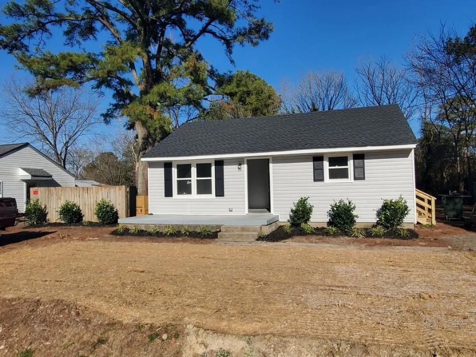 Small, light gray house with black shutters, door, and roof. Lawn and landscaping in front. Sunny day.