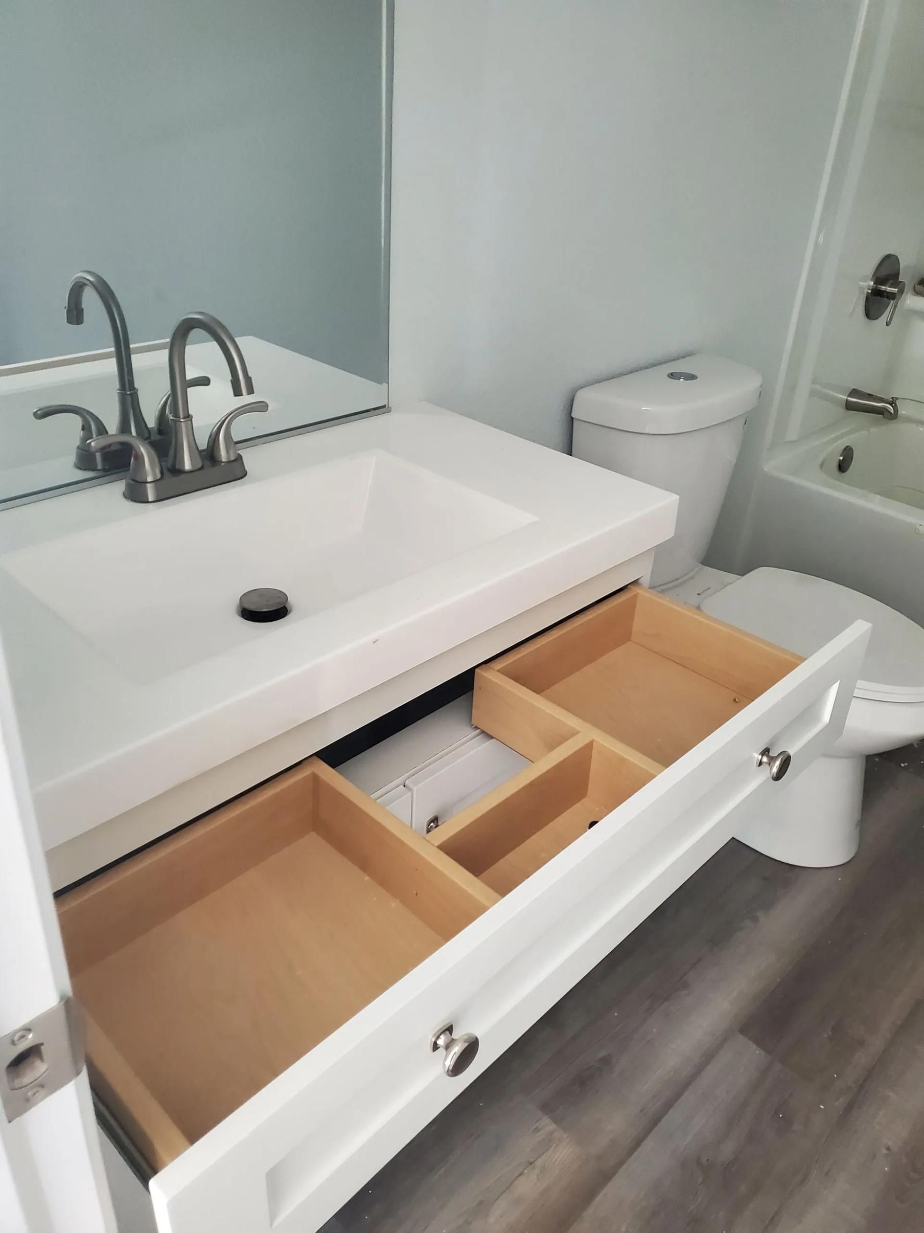 White bathroom vanity with sink, mirror, and open drawer organizers in a modern bathroom.