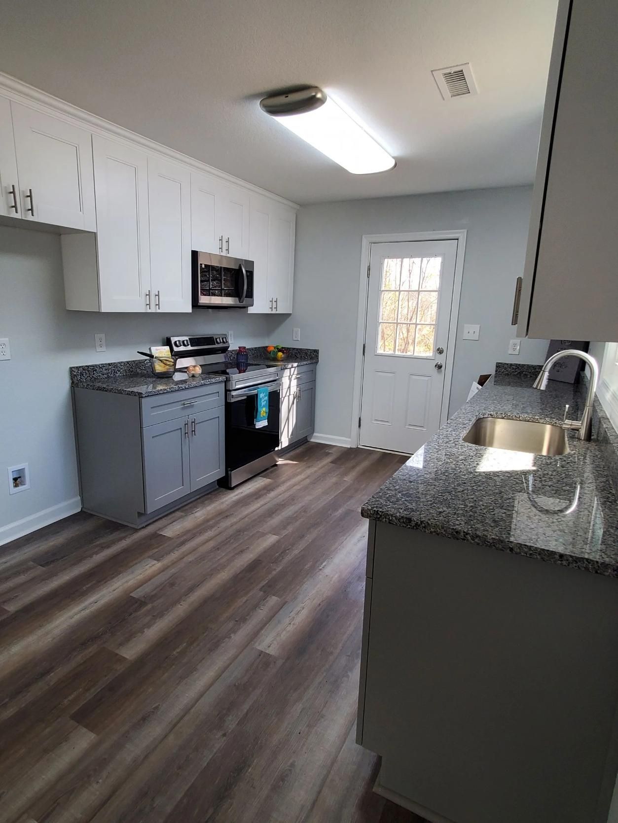 Bright modern kitchen with white cabinets, gray counters, stainless appliances, and wood-look flooring.