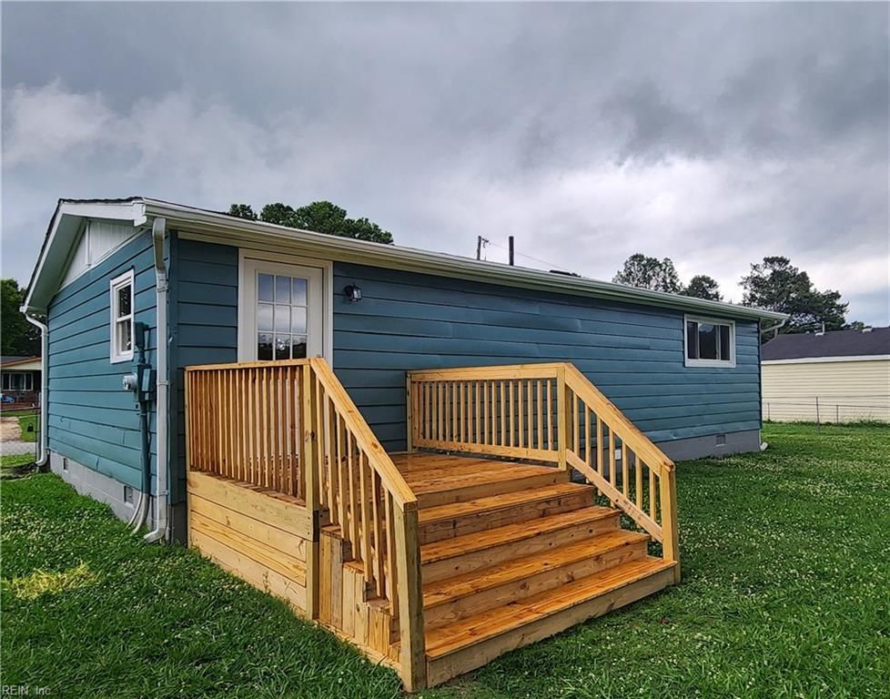 Blue house with wooden deck and stairs; green grass and overcast sky.