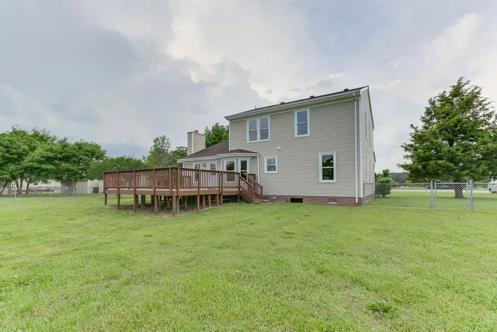 Small gray house with a wooden deck on a grassy lawn under a cloudy sky