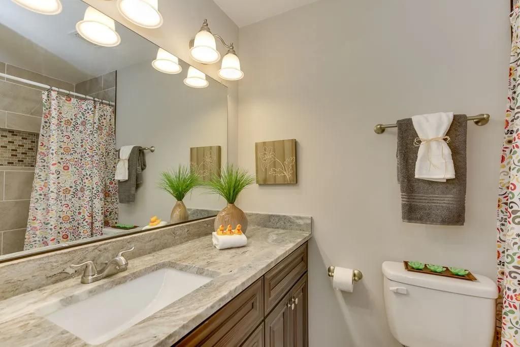Bright bathroom vanity with granite counter, large mirror, and towels on the wall