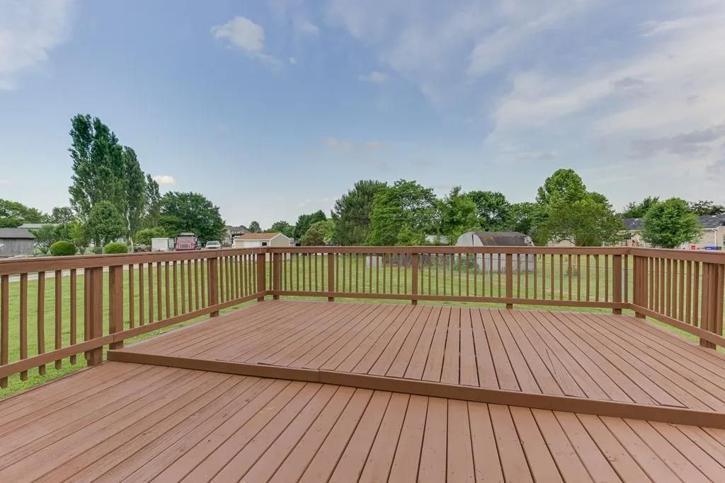 Wooden deck with railing overlooking a green backyard under a cloudy sky