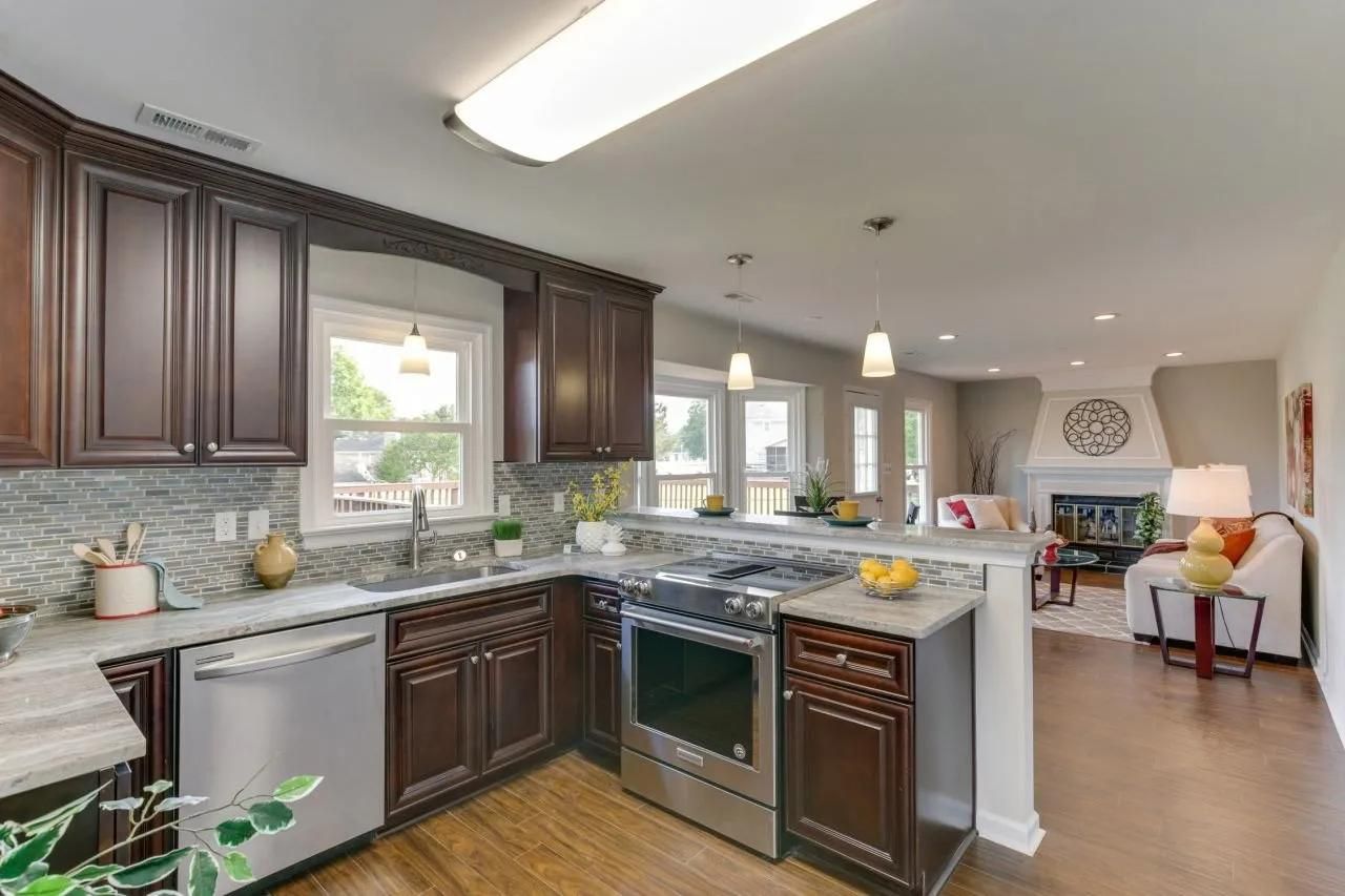 Bright modern kitchen with dark cabinets, granite counters, stainless appliances, and open view to a living room.