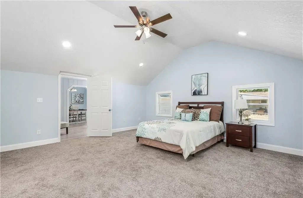Spacious light-blue bedroom with vaulted ceiling, ceiling fan, bed, dresser, and carpeted floor