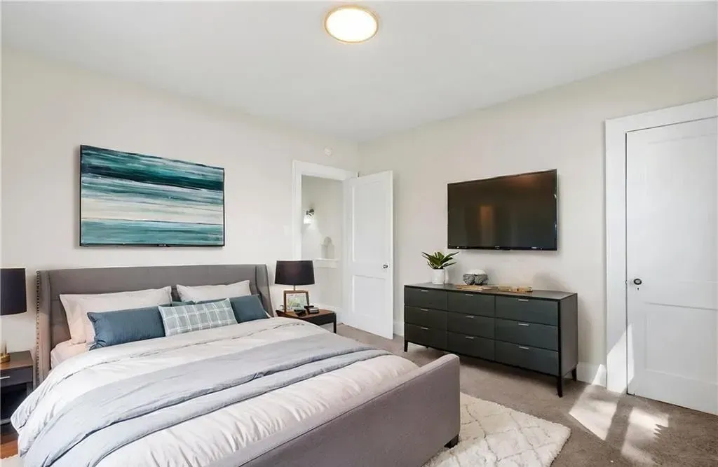 Bright bedroom with a bed, wall art, dresser, TV, and white doors on the right.
