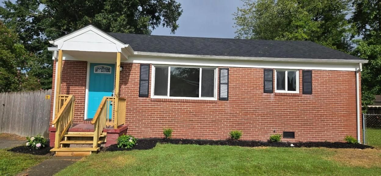 Small brick house with white trim, turquoise front door, and wooden steps in a grassy yard