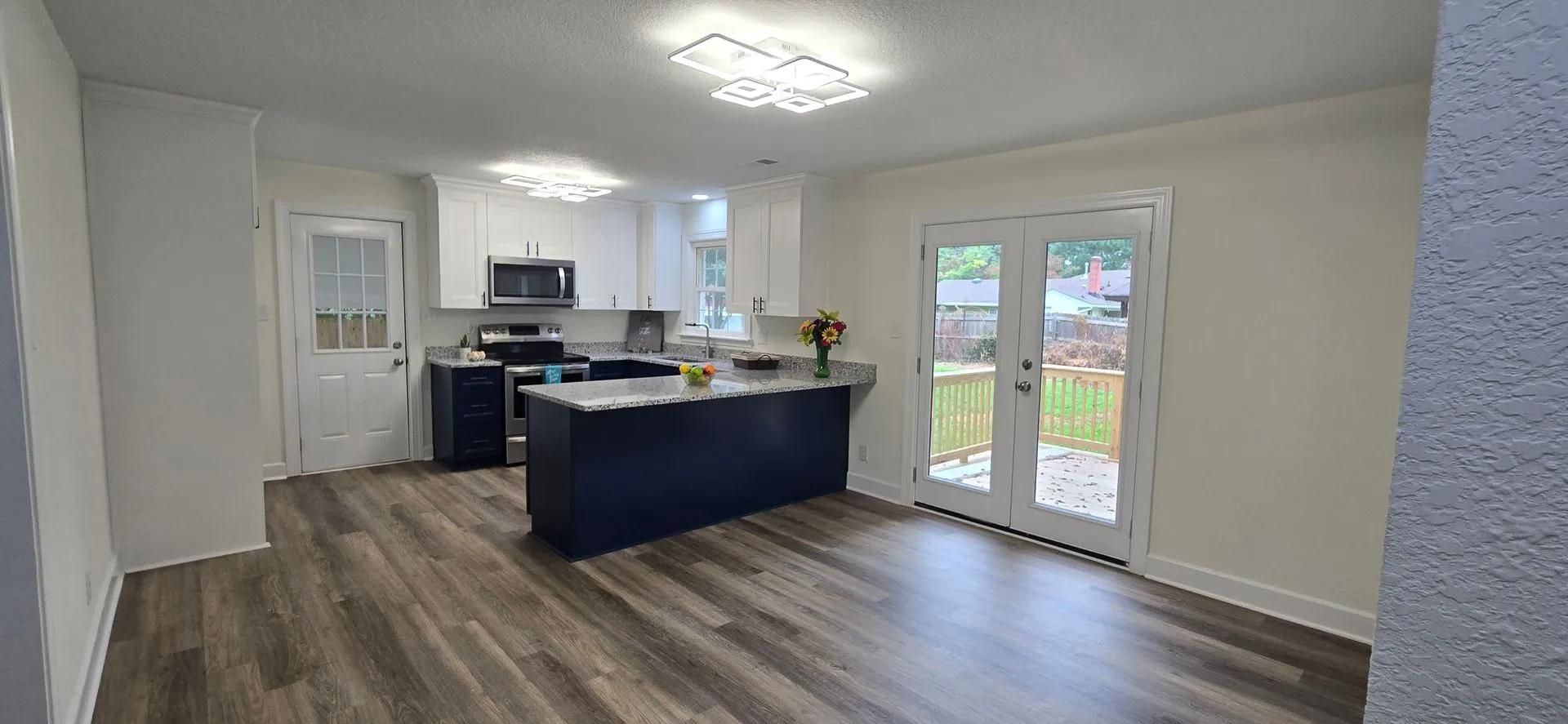 Open-plan kitchen and living area with white cabinets, dark island, and sliding glass doors