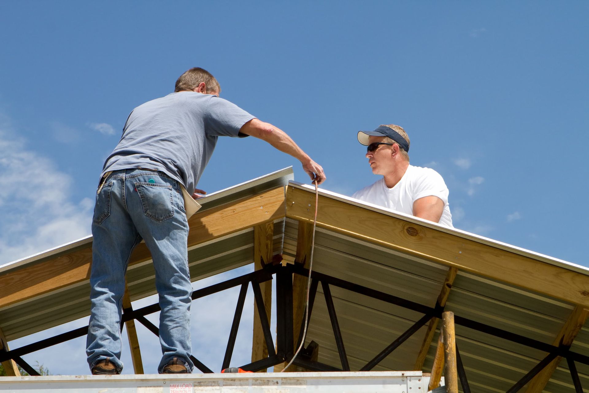 Two people building a roof on a sunny day. One measures, the other looks on.