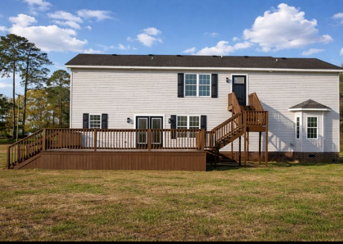 White two-story house with a wooden deck and stairs in a grassy yard under a blue sky