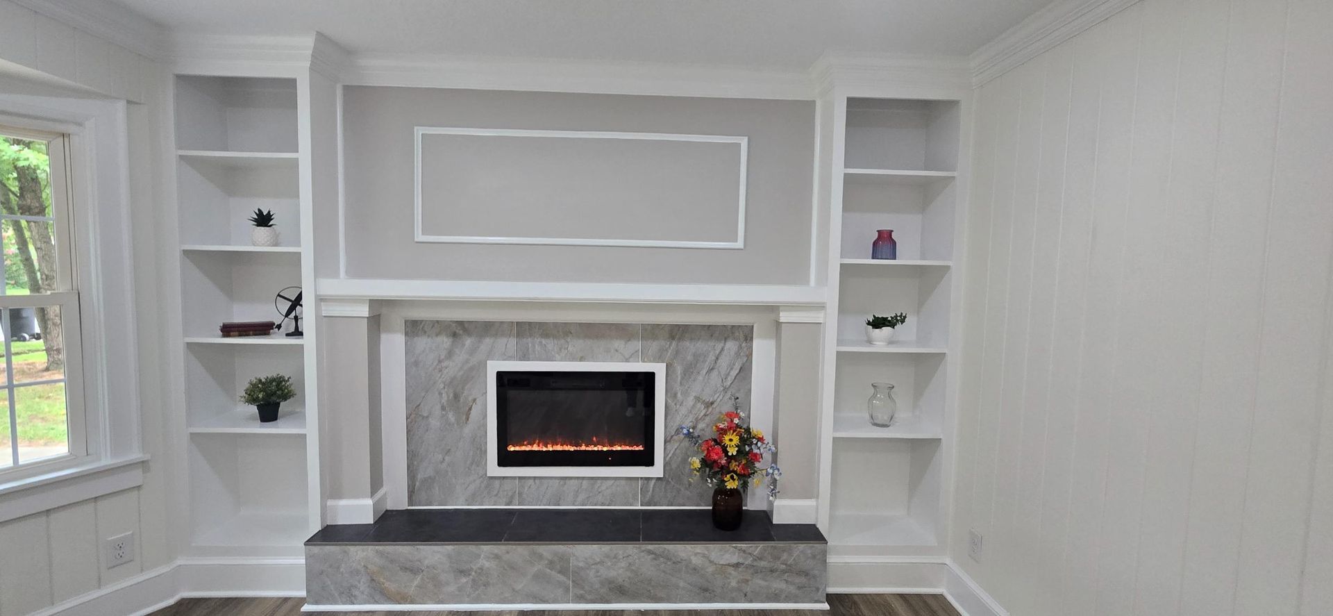 Built-in white shelves flank a gray fireplace with a black electric firebox and decor.