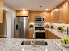 Modern kitchen with stainless steel appliances, wood cabinets, and a marble island with sink and fruit bowl