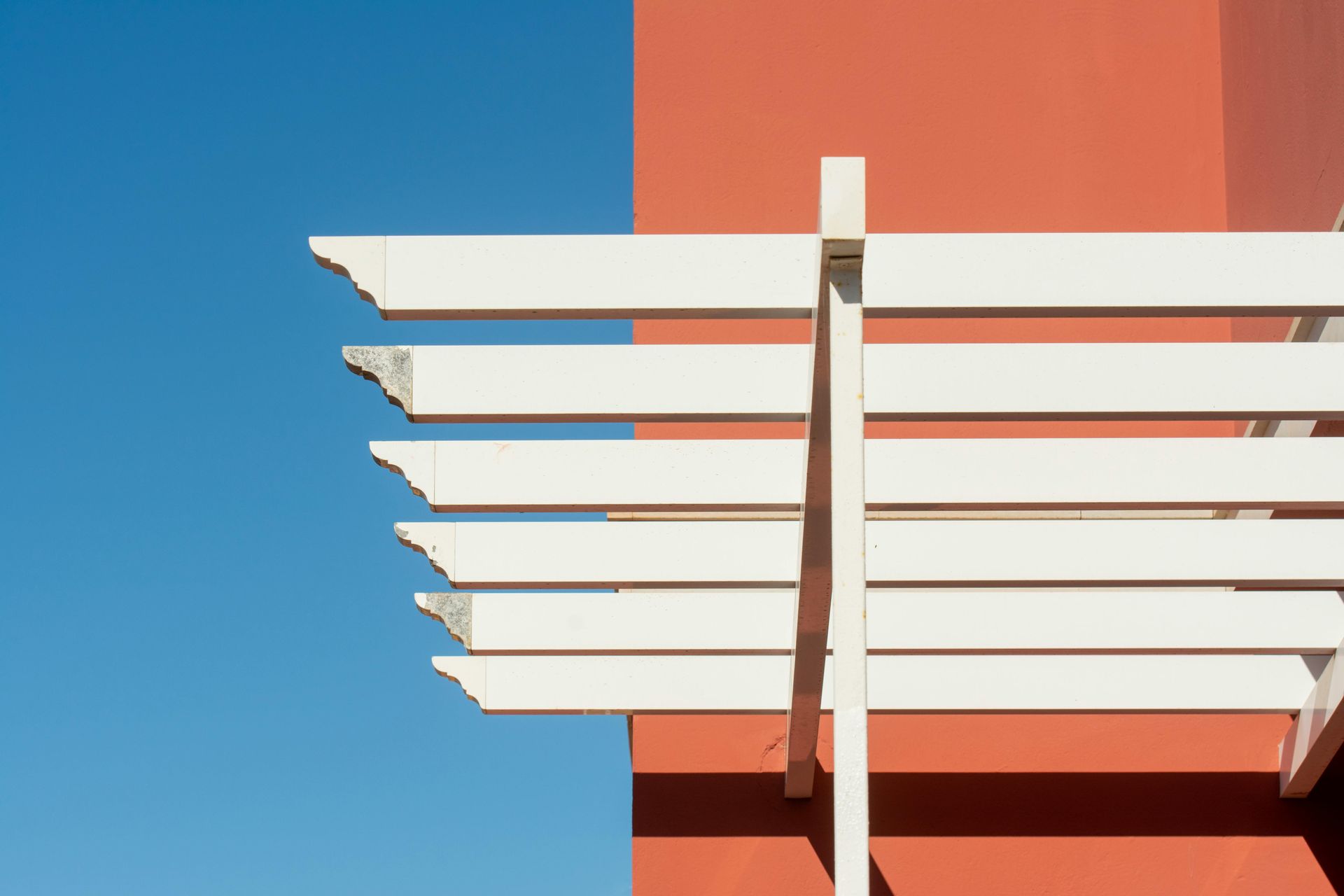 White wooden pergola against a red wall and blue sky.