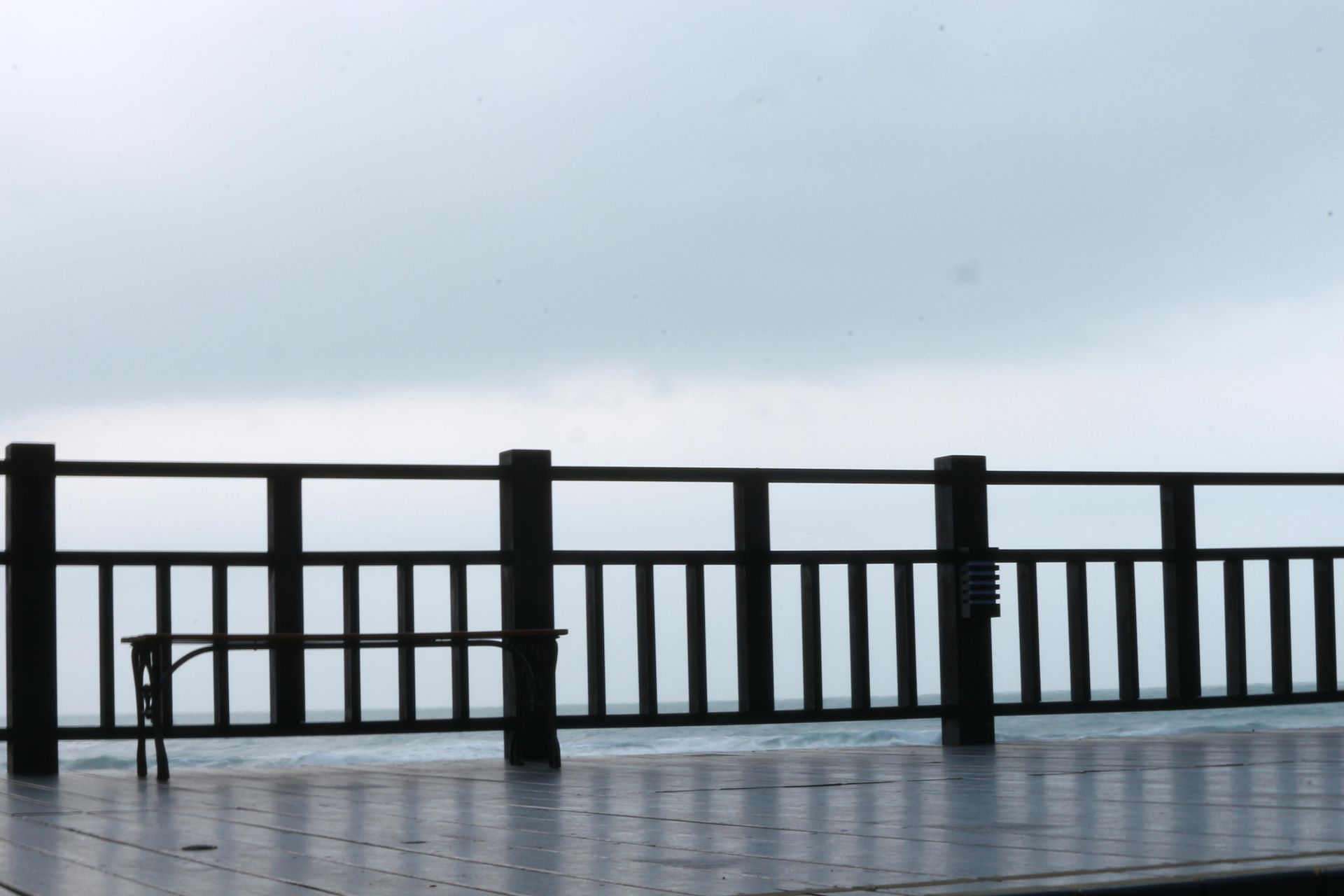 Wooden deck with a railing overlooking a gray, overcast sky and a body of water.