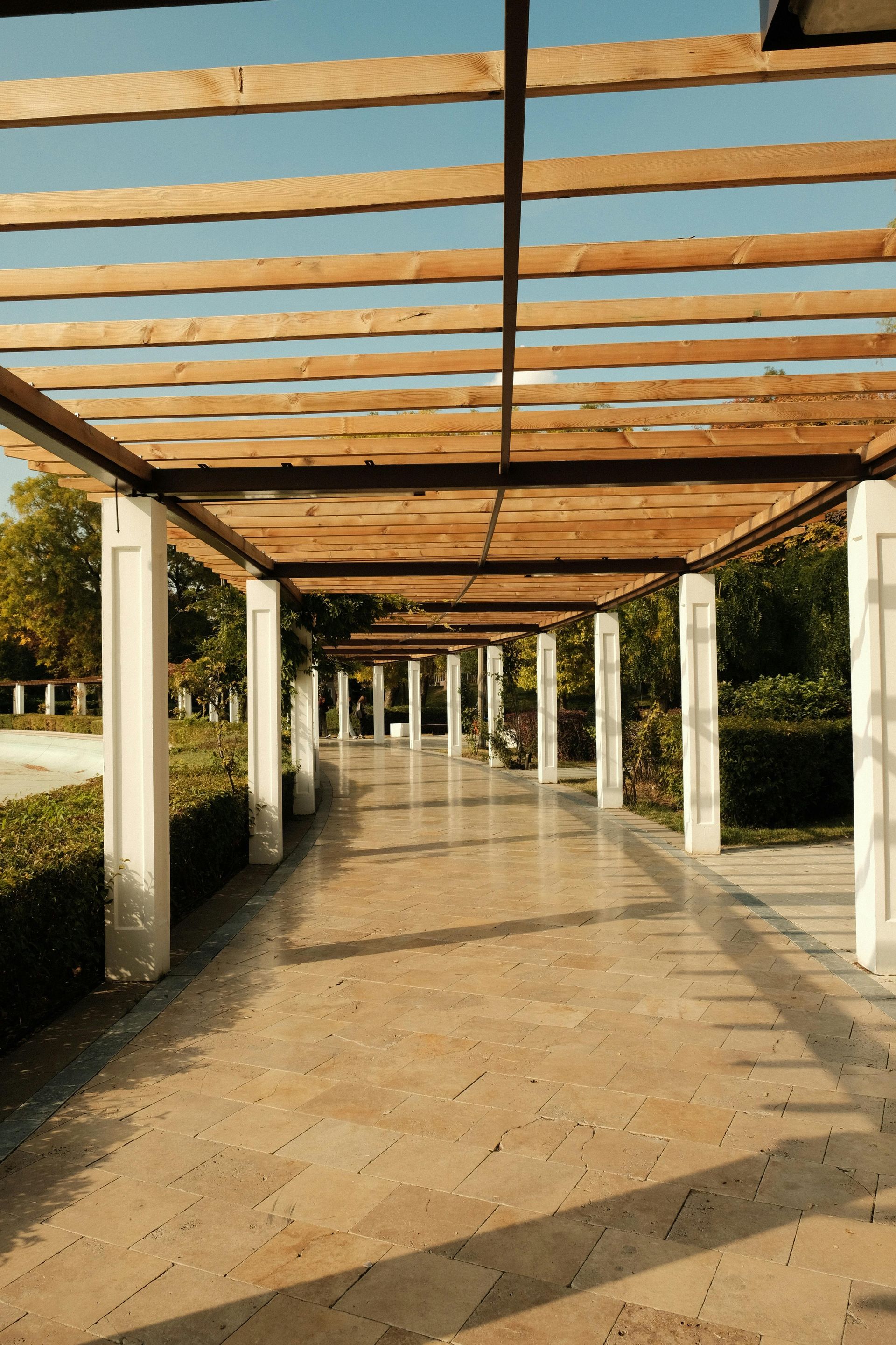 A long, covered walkway with wooden beams, white pillars, and a stone path.
