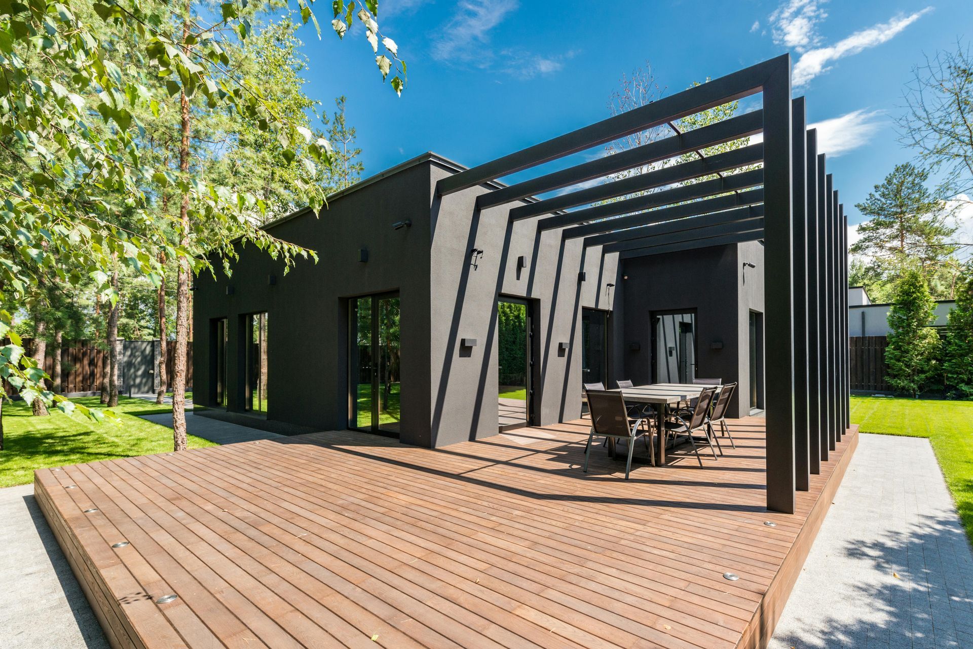 Modern black house with wooden deck, pergola, and outdoor dining area.
