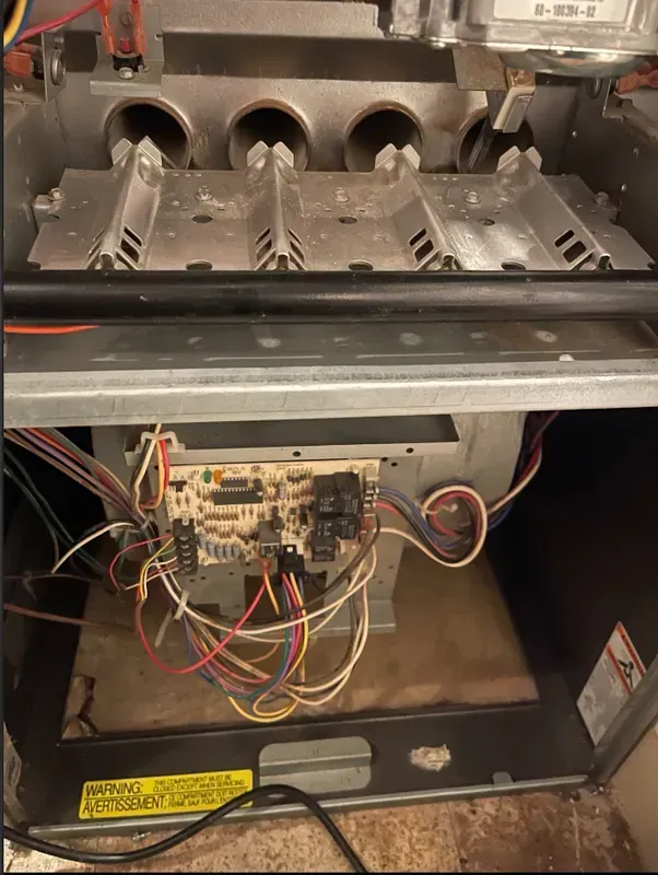 Open furnace compartment with burners above and exposed wiring/control board below
