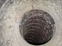 Open circular manhole with a dark, deep shaft in a concrete surface