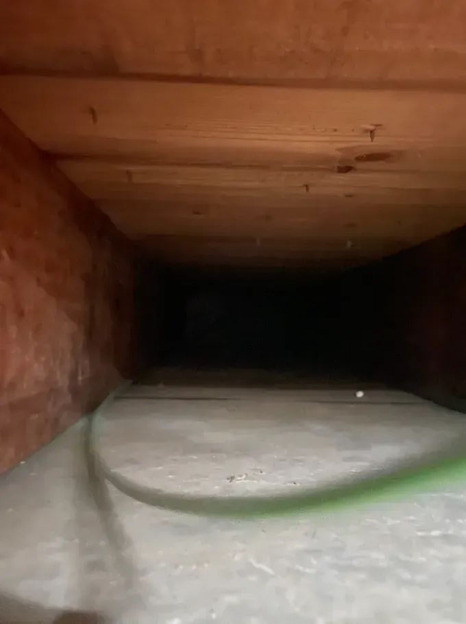 Inside a wooden duct, a white foam object lies on the floor with darkness at the far end.