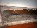 Large wall opening with crumbling plaster and exposed brown insulation in a damaged interior.