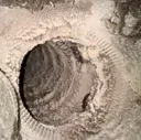 Close-up of a circular hole in light beige sand or soil with ridged edges