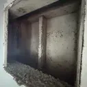 A metal vent or duct opening with heavy dirt and debris buildup inside and along the bottom edge.