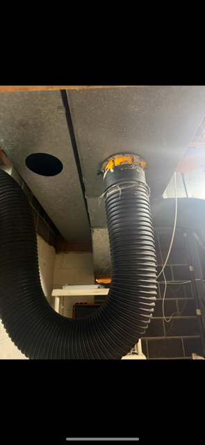 Black corrugated ventilation hose attached to a ceiling vent in an industrial-looking space