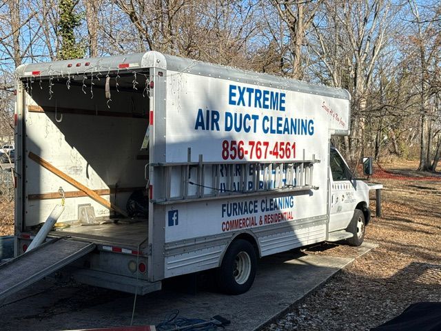 White service truck for Extreme Air Duct Cleaning parked outdoors, rear door open, trees in background