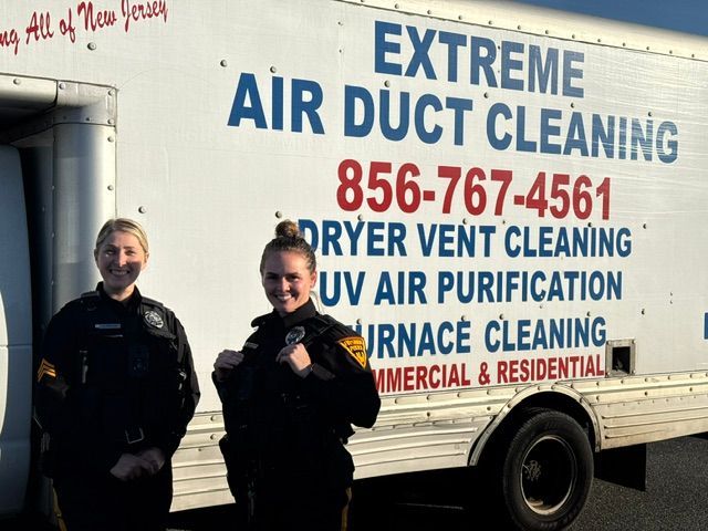 Two people standing beside an Extreme Air Duct Cleaning service van with bold blue and red lettering.