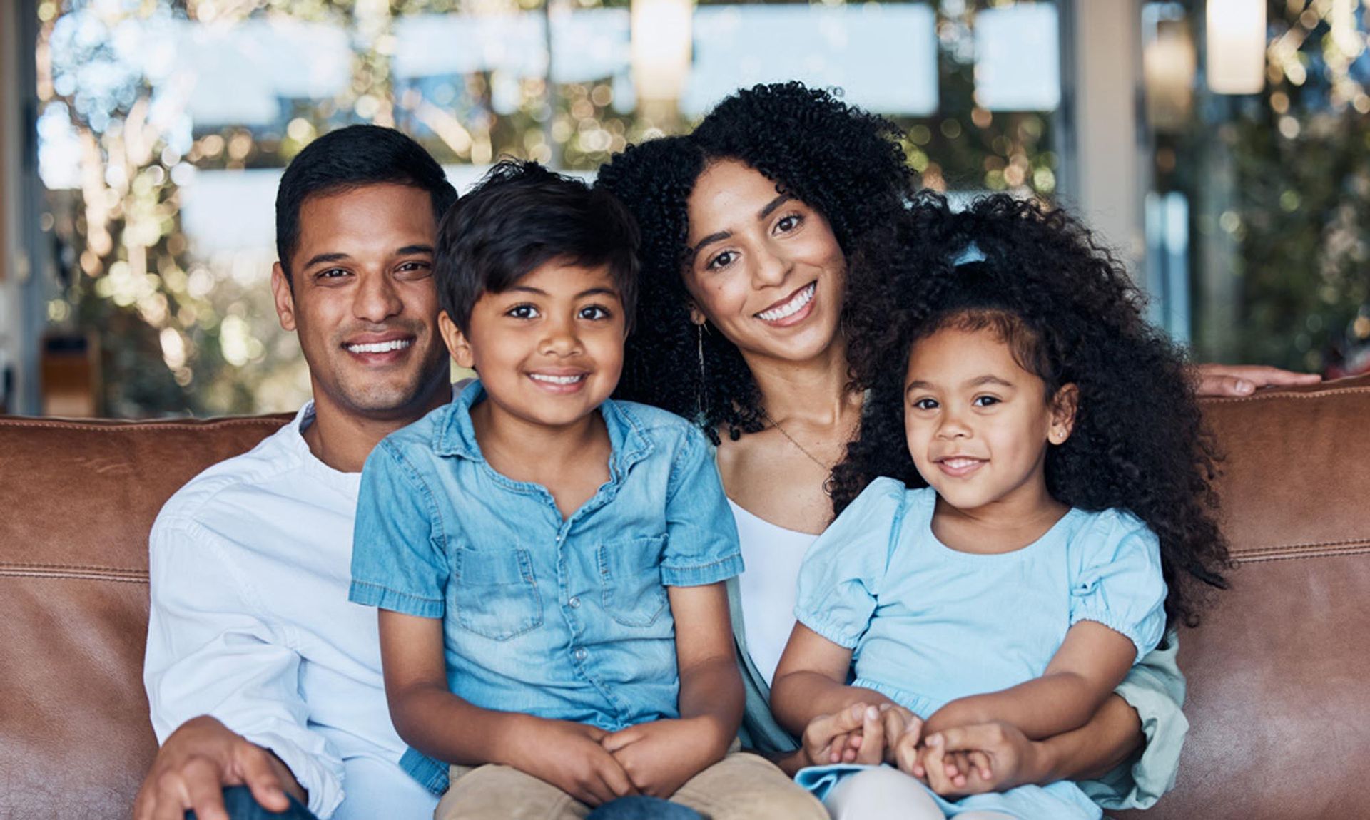 Family of four smiling together on a brown couch.