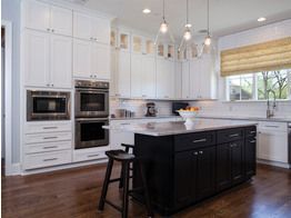 A kitchen with white cabinets and black cabinets and a large island in the middle.