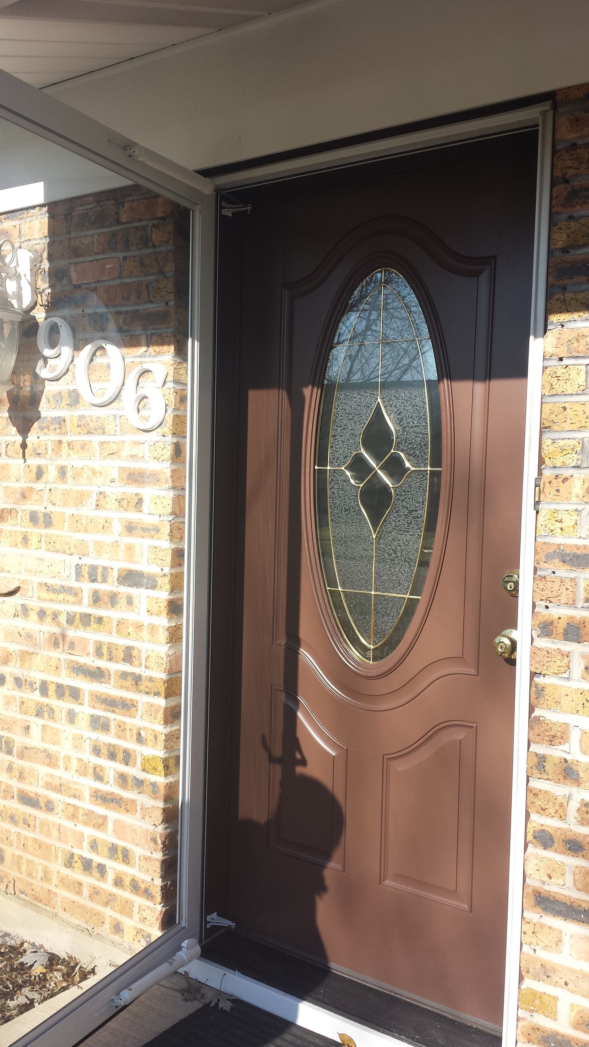 A brown front door with a stained glass window on a brick building.
