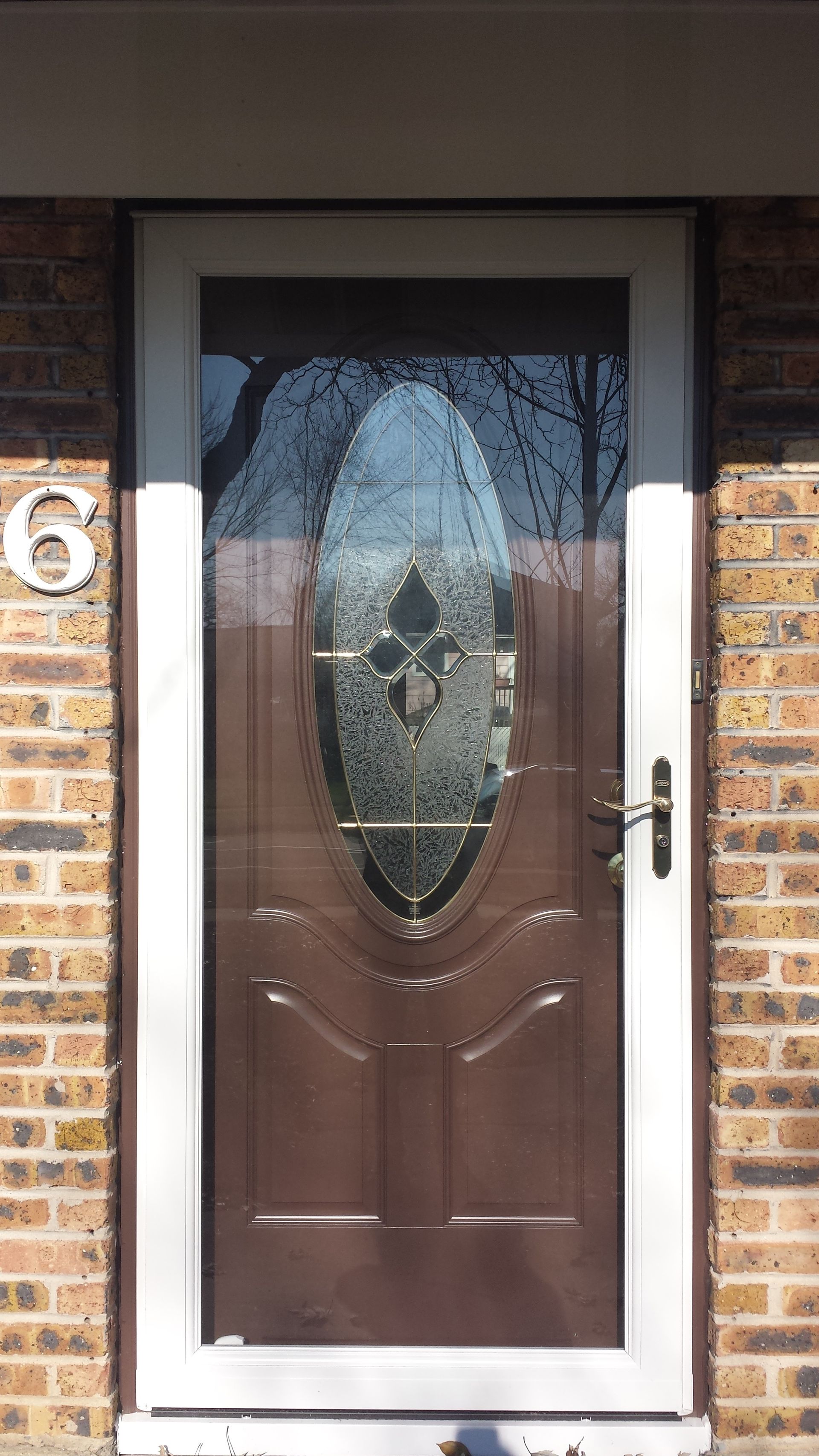 A brown door with a glass window is on a brick building.